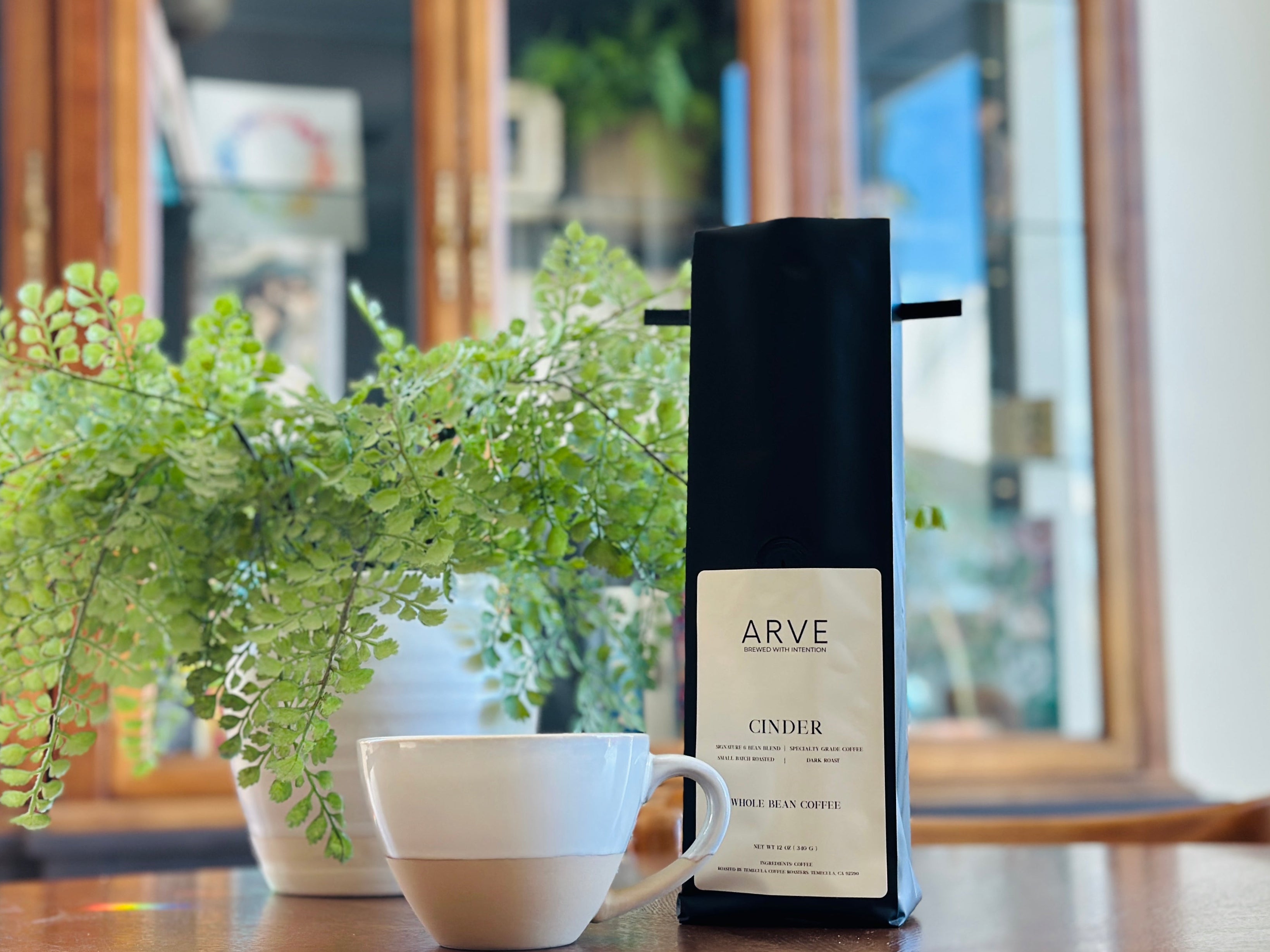 Cup of coffee with a plant and a bottle labeled 'ARVE' on a wooden table.